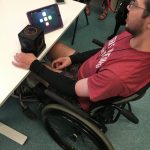 A young man sitting in a wheelchair plays with Skoog and iPad.