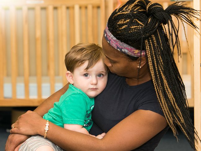 Black woman embracing a young white boy on her lap