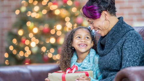 mom and daughter holding gift in front of Christmas tree