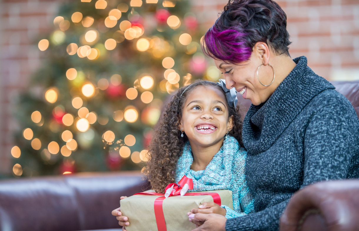 mom and daughter holding gift in front of Christmas tree