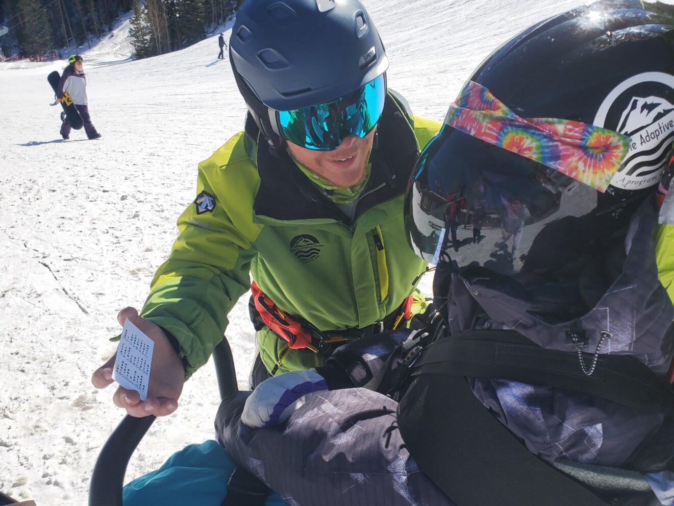 Ski instructor holding up Morse Code card for individual on adaptive ski's.