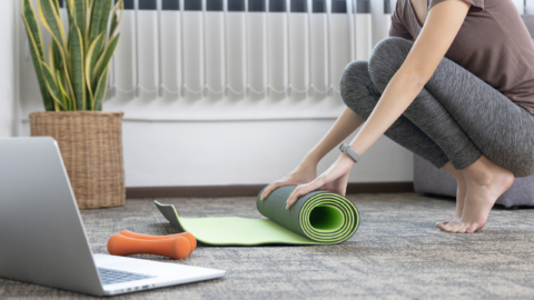 female rolling out yoga mat with laptop in foreground
