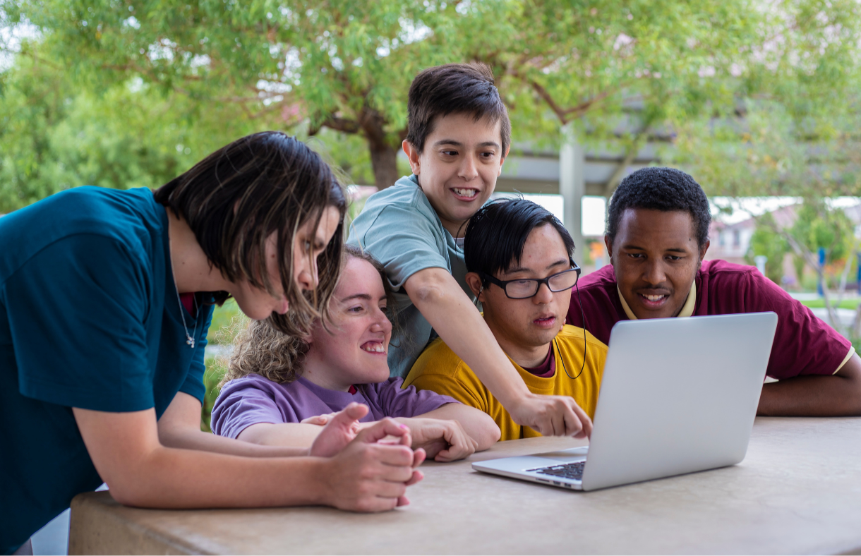 Five friends smiling and looking at a laptop together