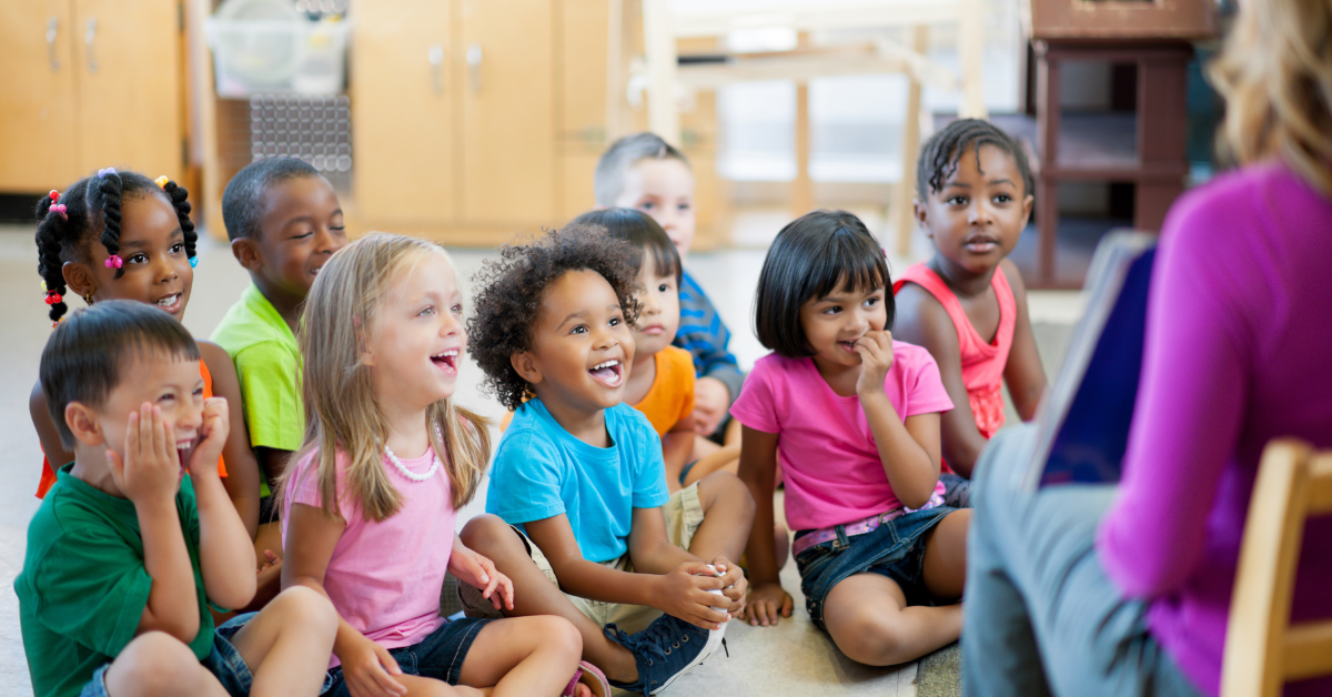 young school children sitting gathered in front of teacher