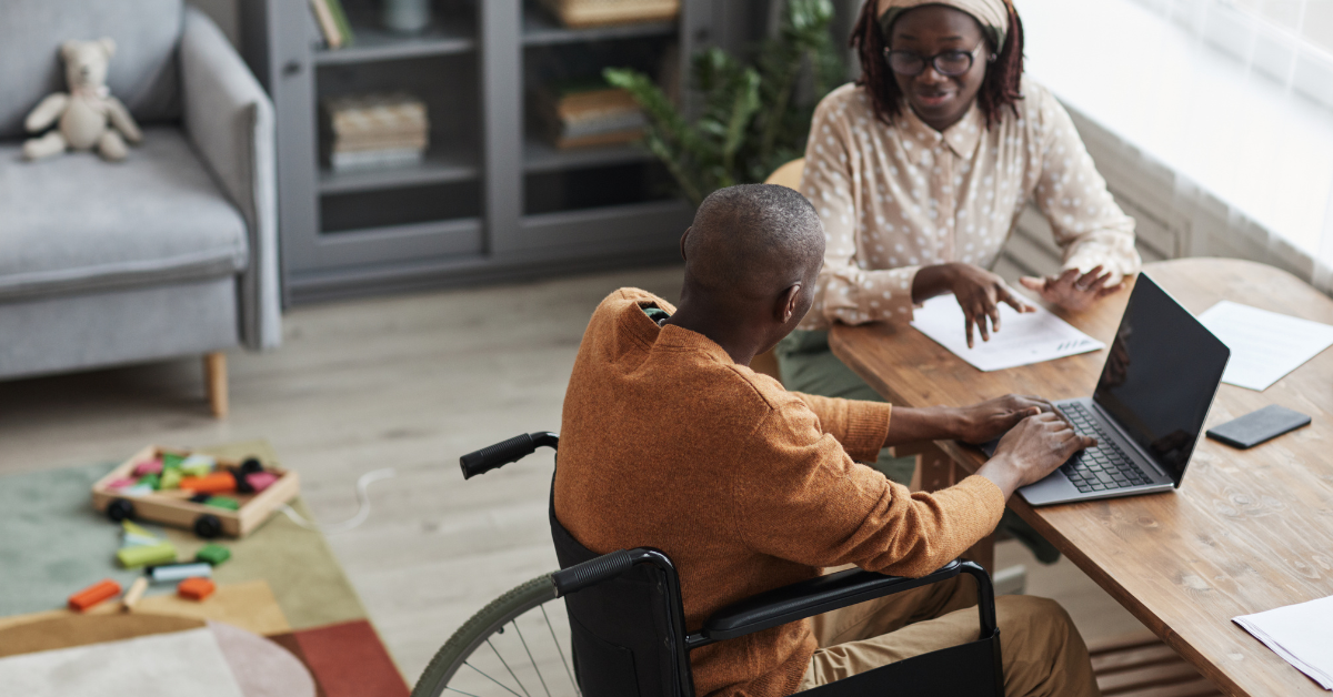 man in wheelchair sitting at table with laptop. female sitting next to him