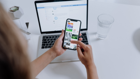 image of hands holding a phone with laptop in background