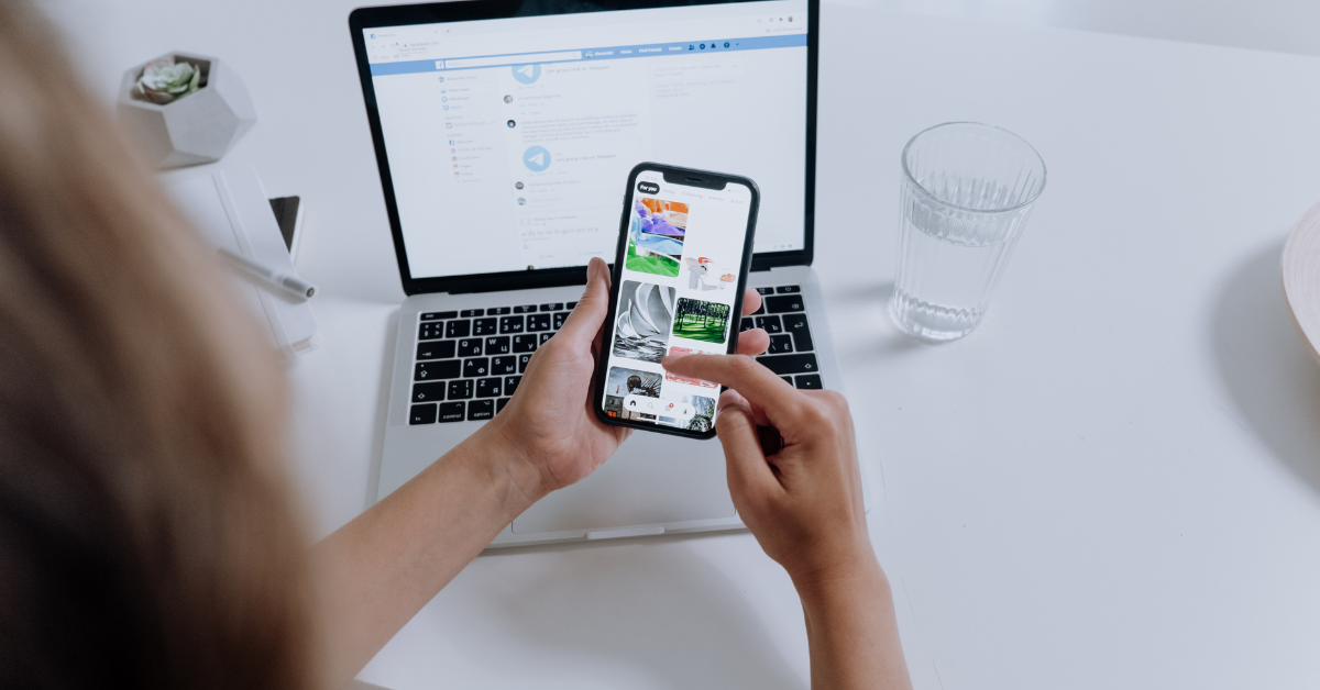 image of hands holding a phone with laptop in background