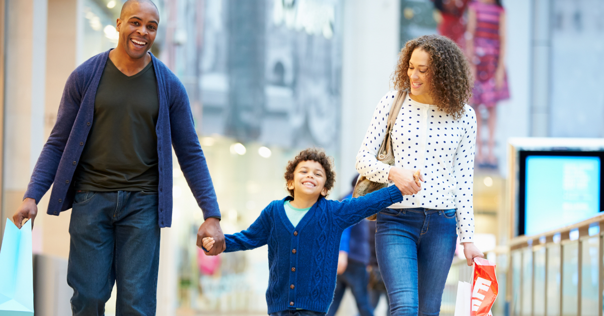 2 adults holding child's hand between them carrying shopping bags