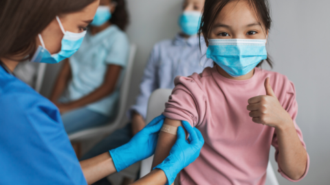 girl wearing a mask giving a thumbs up after getting a vaccine