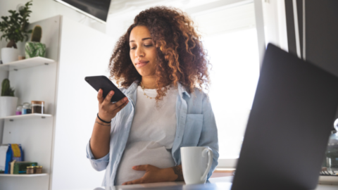 pregnant mom looking at phone while sitting in front of laptop