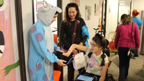 Girl in wheelchair using iPad to communicate picking candy from a halloween bucket