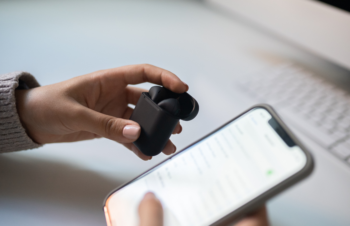 hands holding wireless ear buds and smartphone