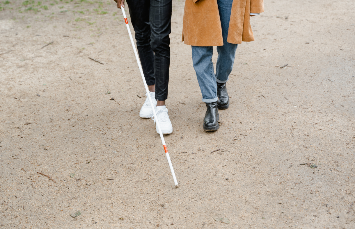 2 people walking together, one with a white cane