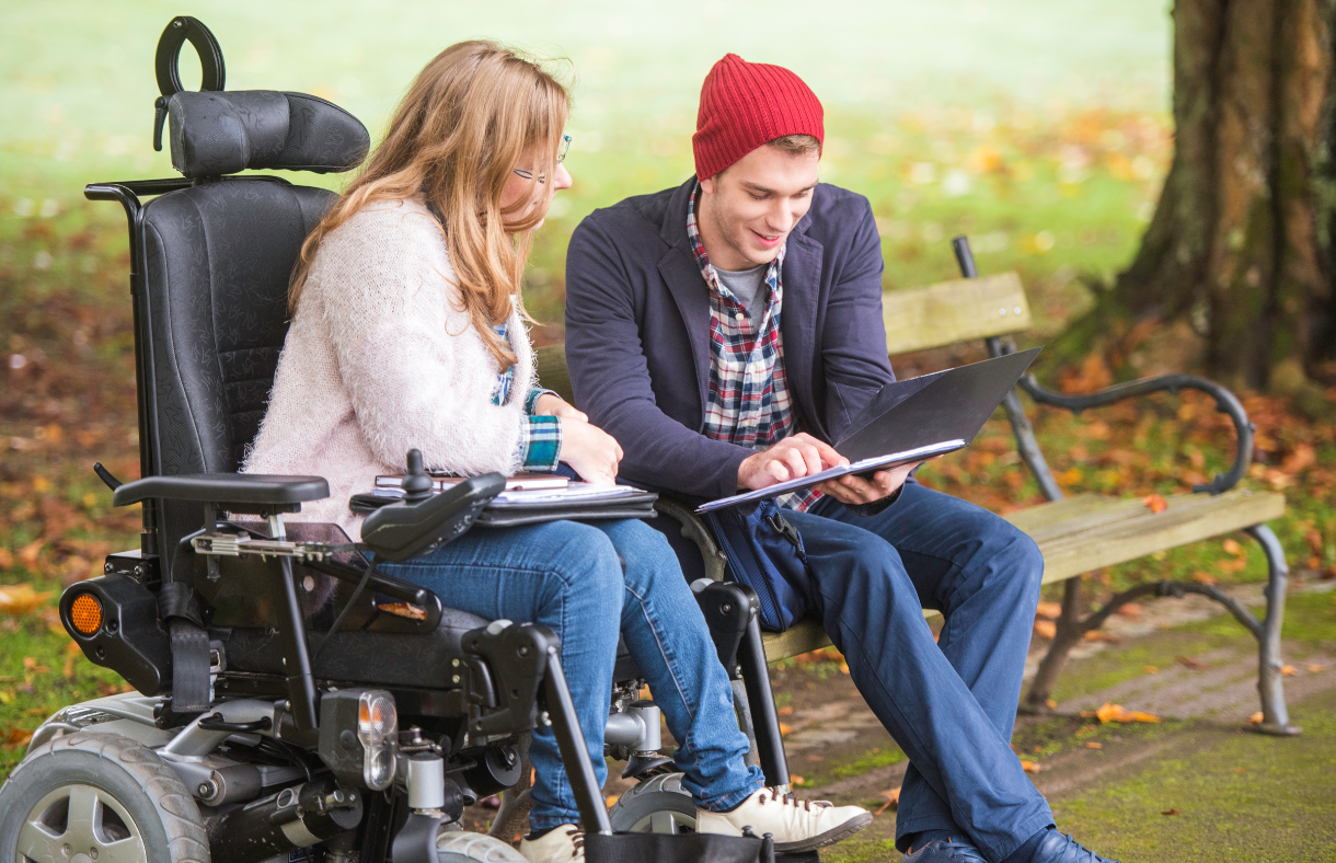 young adult female in wheelchair sitting with male friend. both looking at mobile device