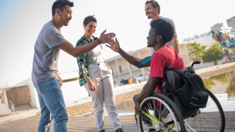 friends giving a high five to young adult male in wheelchair