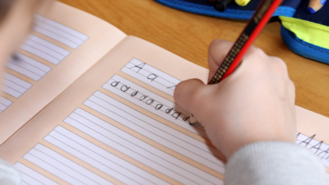 student's hand practicing writing letters