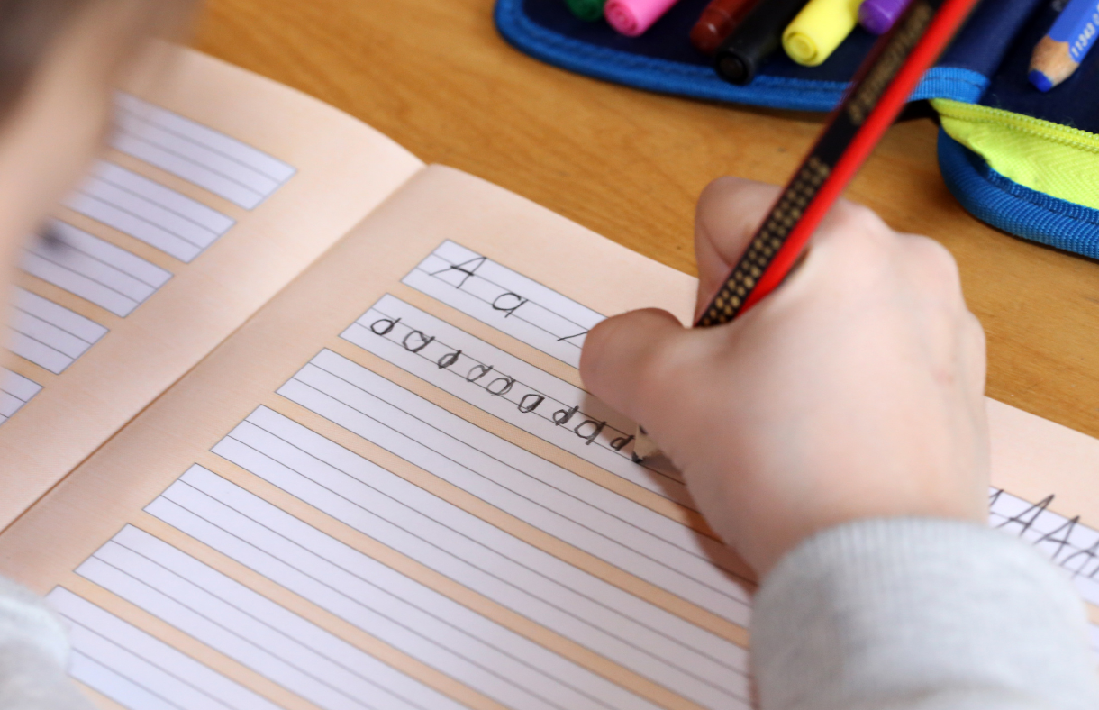 student's hand practicing writing letters