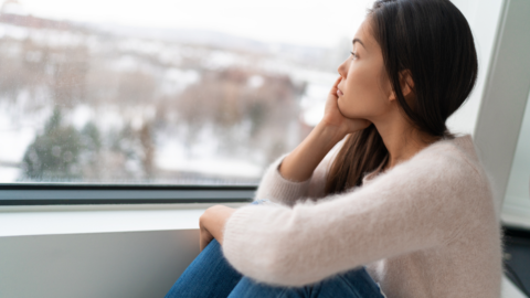 lady sitting beside window looking sad. dismal snowy day outside