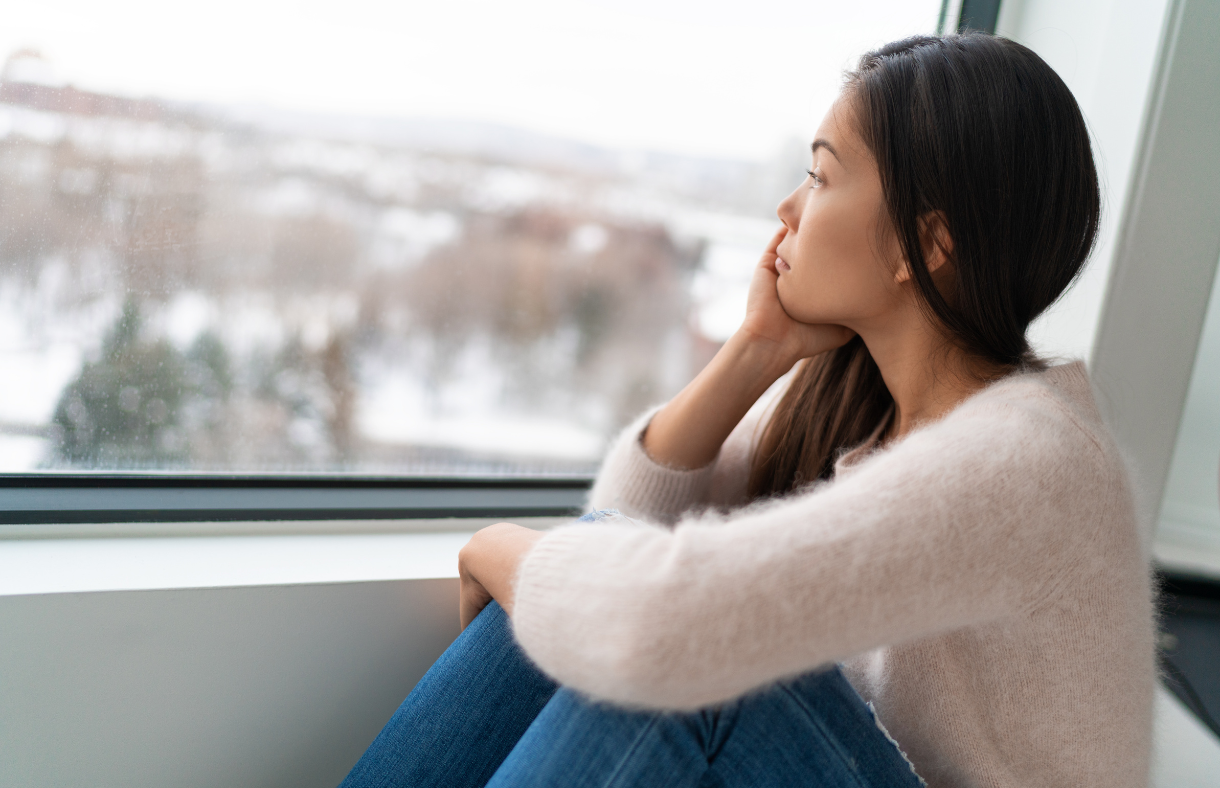 lady sitting beside window looking sad. dismal snowy day outside