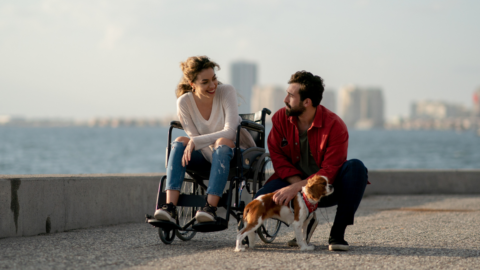 woman in wheelchair with male friend kneeling while walking dog
