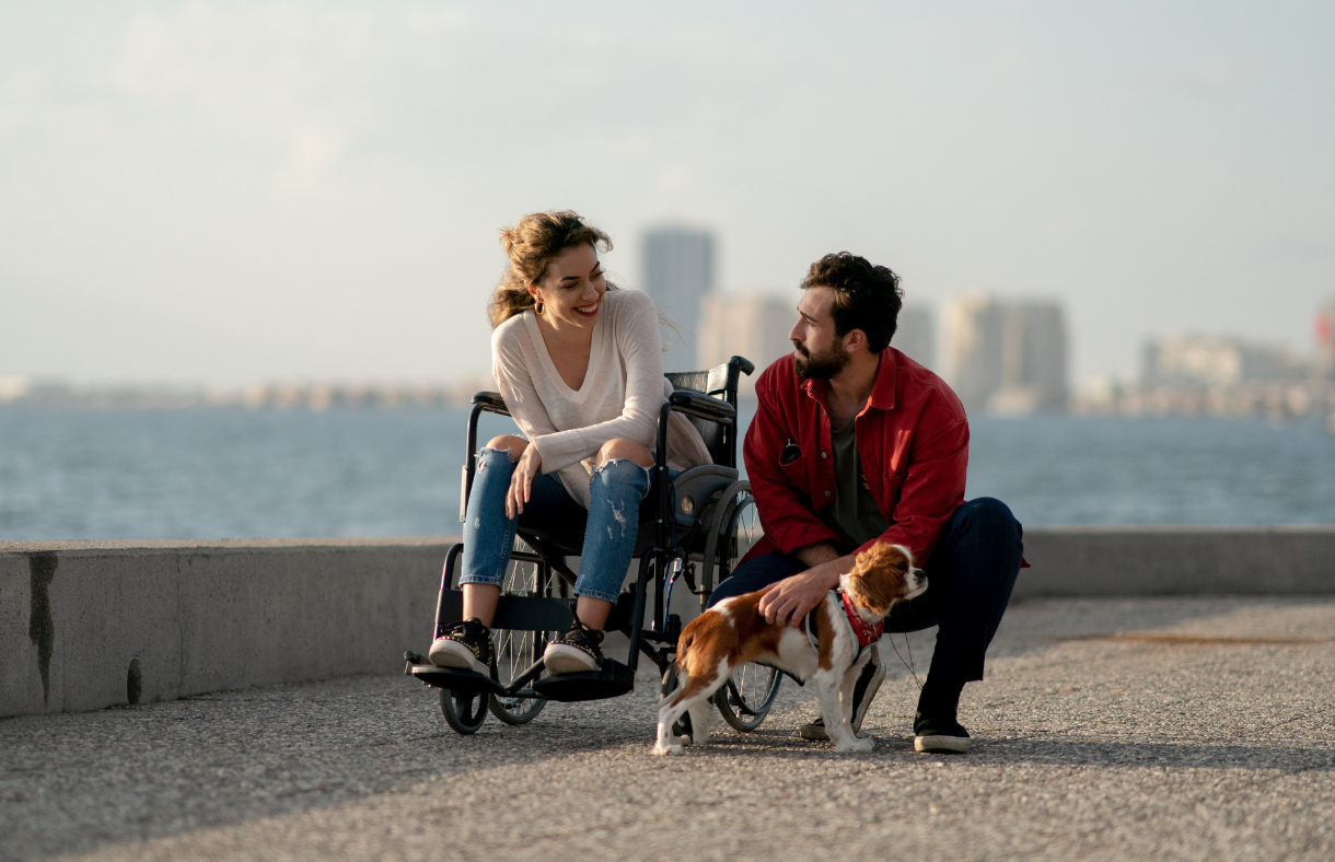 woman in wheelchair with male friend kneeling while walking dog
