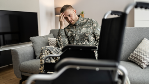 man in military uniform sitting next to wheelchair holding head