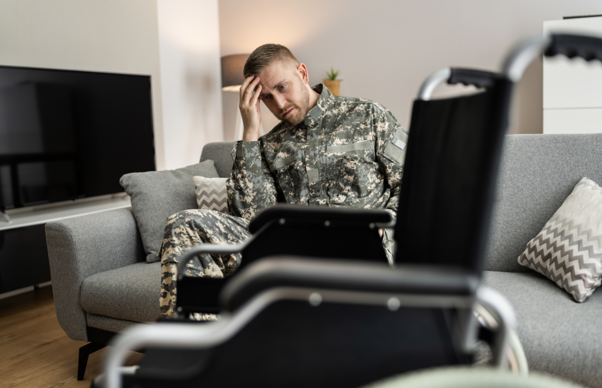 man in military uniform sitting next to wheelchair holding head