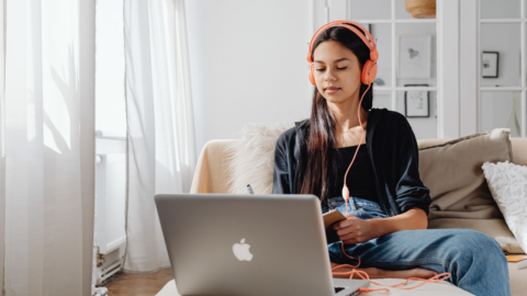 teen girl with headphones on looking at macbook