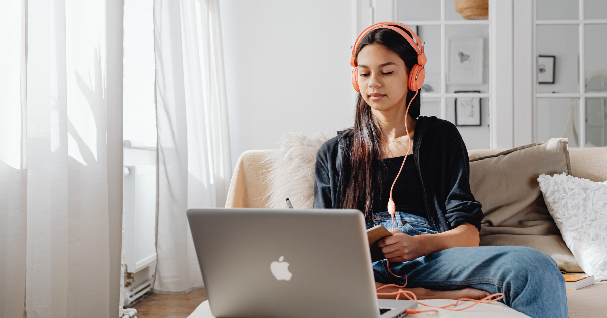 teen girl with headphones on looking at macbook