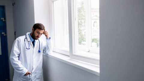 male doctor with head resting in hand looking out window
