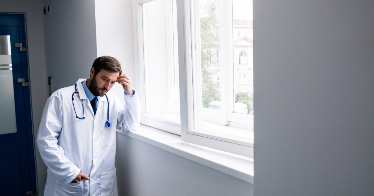 male doctor with head resting in hand looking out window