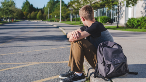 teen boy sitting on curb looking down road