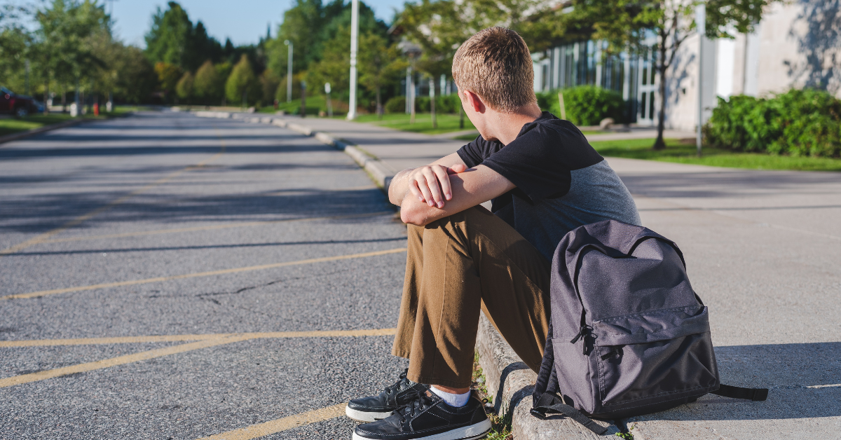 teen boy sitting on curb looking down road