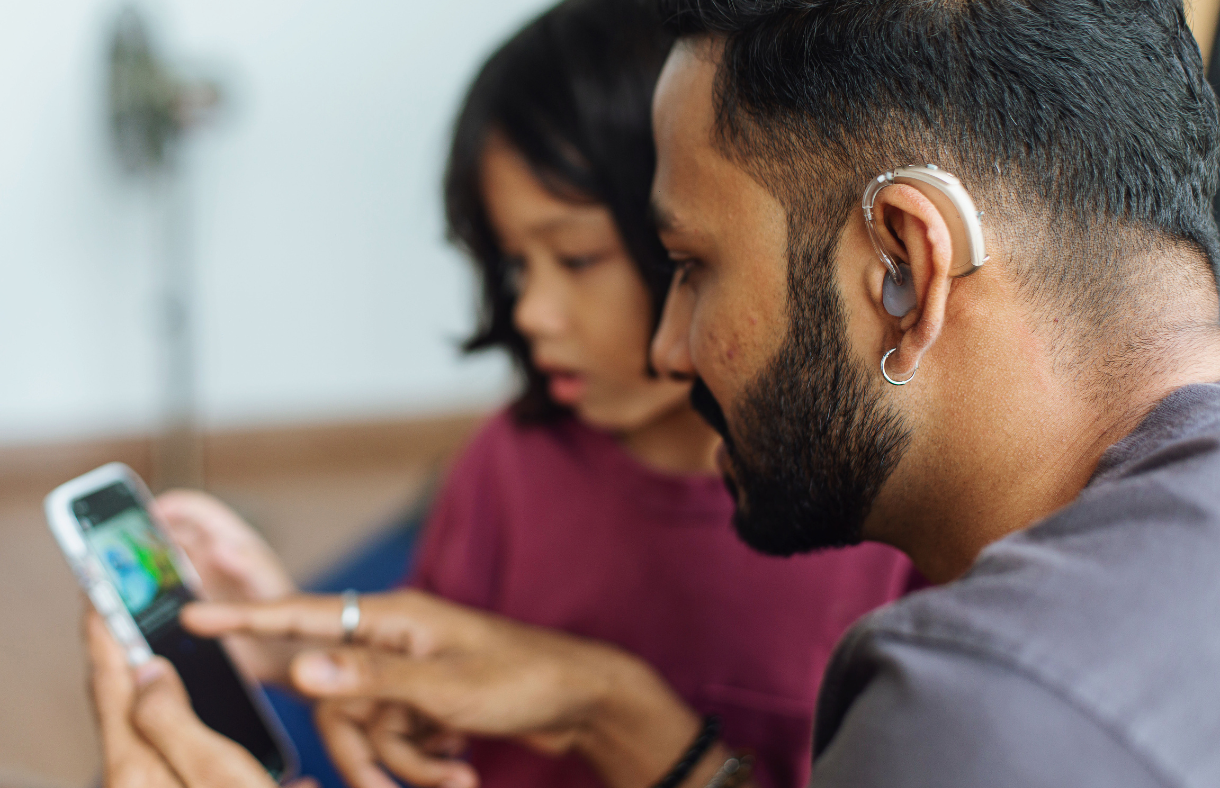 man with hearing aid using phone sitting next to daughter