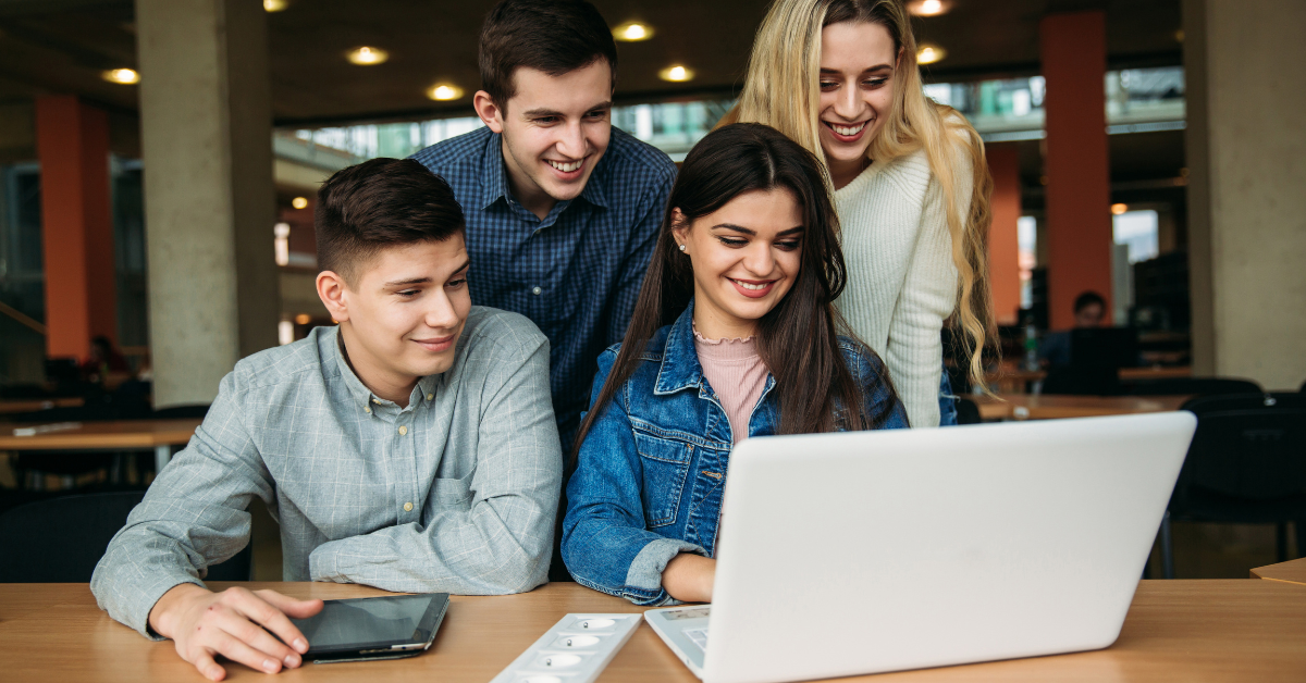 4 college students using laptop together in library