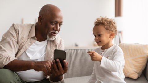 older adult man using pone with young grandchild