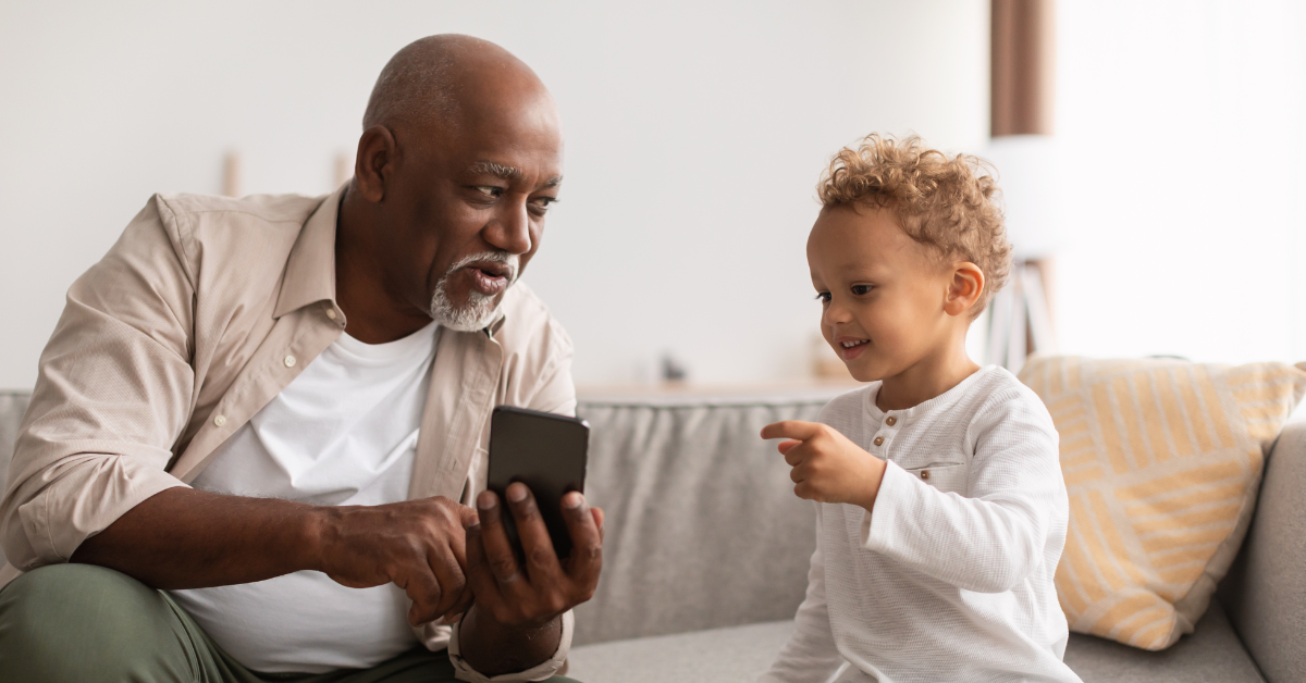 older adult man using pone with young grandchild