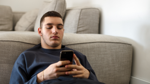 young man sitting on floor leaning against couch looking at phone