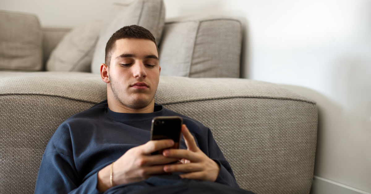 young man sitting on floor leaning against couch looking at phone