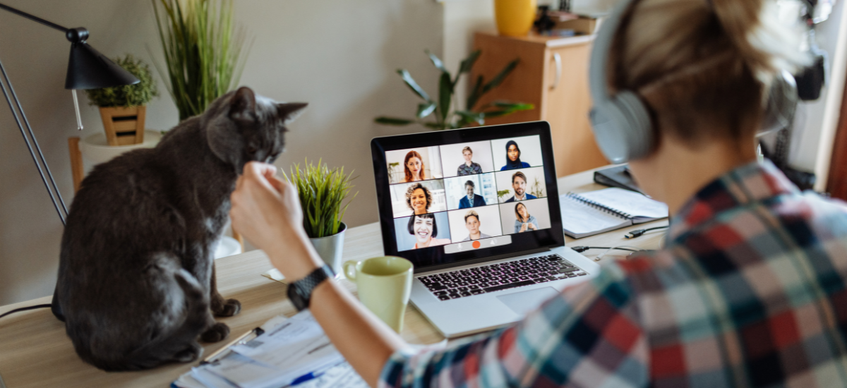 woman on video call with cat sitting on desk next to laptop