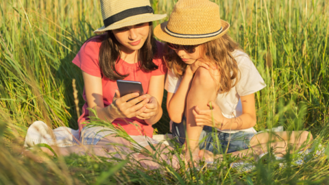 two girls sitting in grass looking at phone together