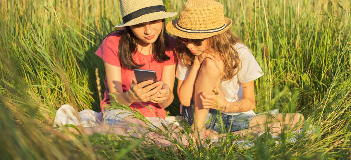 two girls sitting in grass looking at phone together