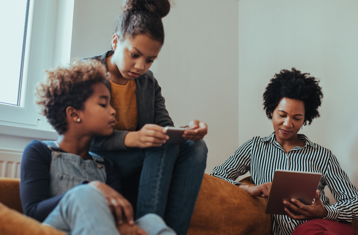 mom and 2 pre-teens sitting together on couch, all using technology