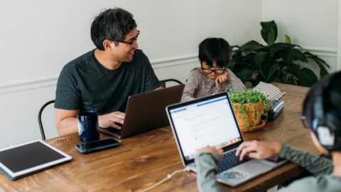 father and two sons sitting at table using technology