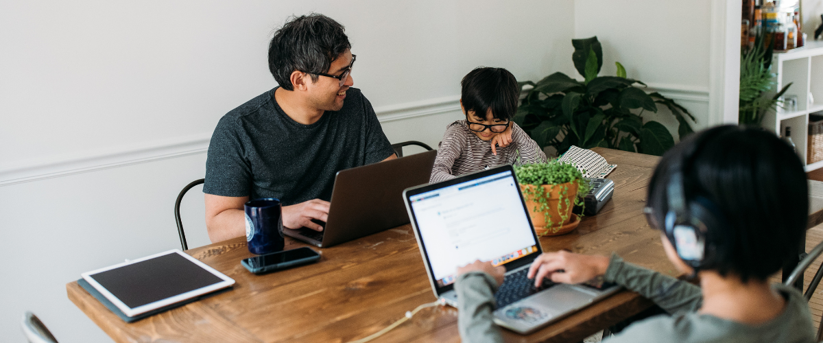 father and two sons sitting at table using technology