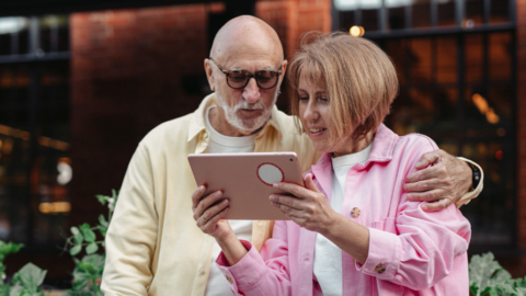 older adult couple standing outside looking at ipad together