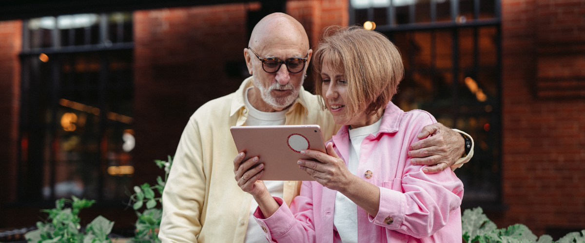 older adult couple standing outside looking at ipad together