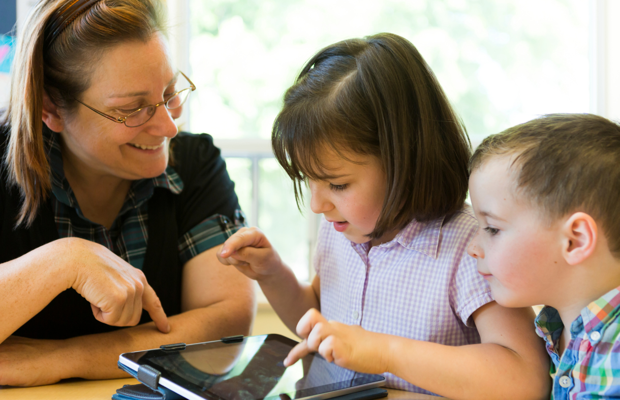 teacher helping 2 young kids with ipad