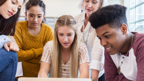 students and teacher gathered around a laptop at table