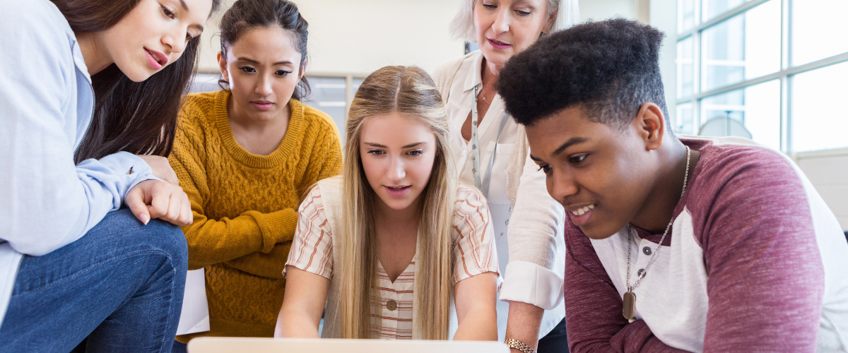 students and teacher gathered around a laptop at table